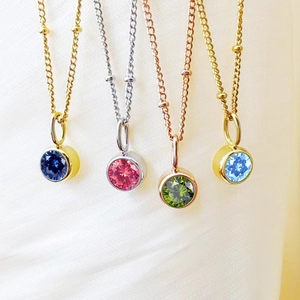 Close-up of sparkling round birthstone pendants on beaded chains in multiple gold finishes