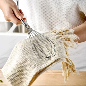 Mini stainless steel spring whisk being held by hand over a beige linen cloth