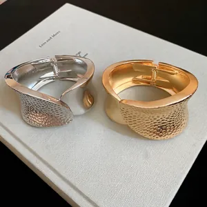 Irregular hammered metal oval cuff bracelet in gold and silver finishes with hinged clasp