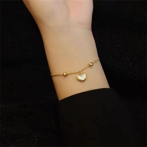Close-up of a 18K gold heart pendant bracelet with white shell inlay on a model's wrist