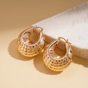 Close-up of golden C-shaped hoop earrings with geometric diamond textured finish