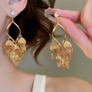 Detailed view of golden leaf tassel earrings with clear zircon on model's ear
