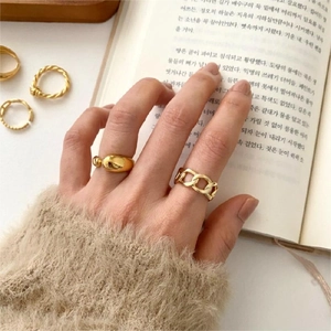 Close-up of golden chain and egg-shaped rings worn on hand against a book background