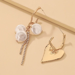 Détail de boucles d'oreilles asymétriques avec perles, strass et cœur doré