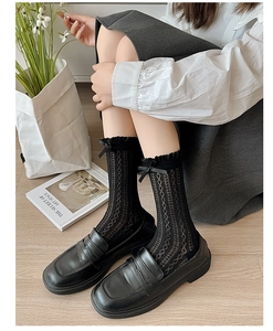 Detail of black hollow mesh socks with lace trim and bow knot worn with loafers