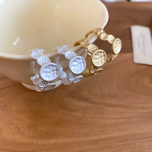 Detail of irregular C-shaped hammered metal earrings in white and gold on a ceramic bowl