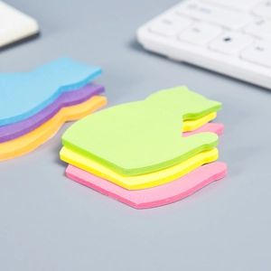 Close-up of cat-shaped sticky notes in green, yellow, and pink on a minimalist desk
