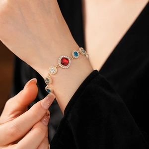 Detailed close-up of a luxury gold bracelet featuring red, blue, and grey gemstones