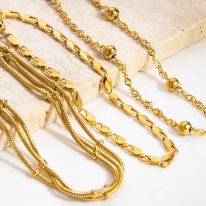 Detailed close-up of stacked 18K gold-plated stainless steel snake and ball chain jewelry