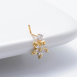 Close-up of golden flower nose stud with clear zircon stones on a white stand