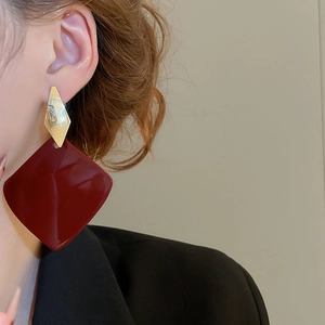 Close-up of geometric earrings with wine red resin diamond pendants worn by a model