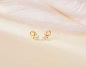 Detailed view of elegant gold knot pearl stud earrings on a minimalist beige background