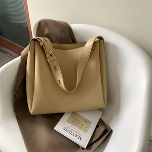Light yellow faux leather tote bag on white chair with artistic book and cozy scene