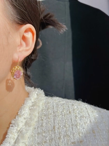 Close-up of golden drop earring with purple gemstone on ear showing elegant design
