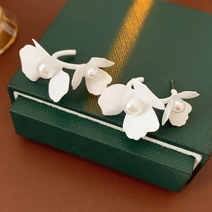 Close-up of elegant C-shaped white floral earrings with pearls on a green jewelry box
