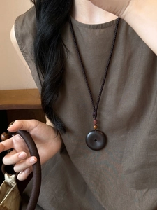 Detalle del collar con colgante de madera hueca y cuerda tejida de estilo étnico
