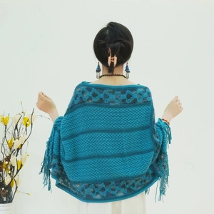 Detail of teal knitted poncho showing geometric diamond patterns and fringe hem for women