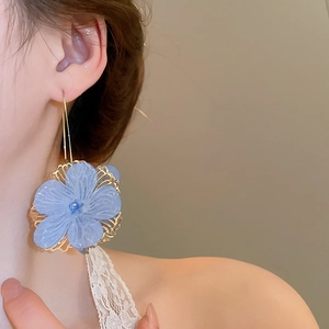 Détail de grandes boucles d'oreilles fleurs bleues 3D avec crochets dorés sur modèle