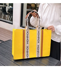 Detail of yellow felt tote bag with MOMPICK letter print handles on textured background