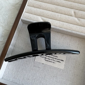 Close-up of a glossy black hair claw clip presented in a premium beige wooden jewelry box
