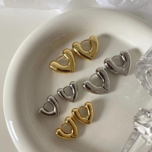 Polished heart-shaped hoop earrings in gold and silver finish on white ceramic plate