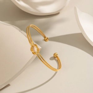 Minimalist knot open bangle in 18K gold-plated stainless steel on artistic stone blocks