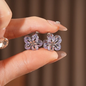 Gros plan de boucles d'oreilles fleurs avec zircons violets tenues à la main