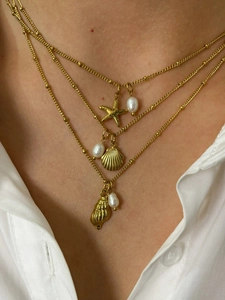 Detail of layered gold necklace with starfish shell charms and white pearls on a model