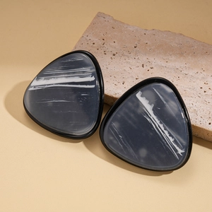 Minimalist resin triangle stud earrings with dark grey marble texture on travertine