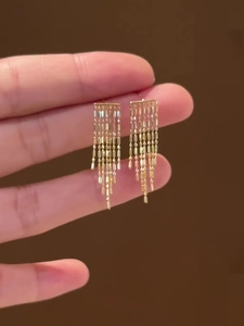 Gros plan de boucles d'oreilles à pompons dorés avec plusieurs chaînes pendantes