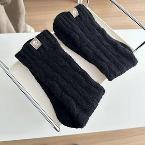 Detailed texture of black ribbed knit wool warmers with a minimalist logo patch