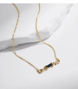 Detail of gold necklace with a blue rectangular gemstone and sparkling side diamonds