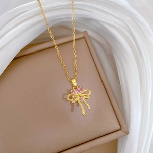 Golden bow necklace with a pink heart gemstone on soft silk fabric background