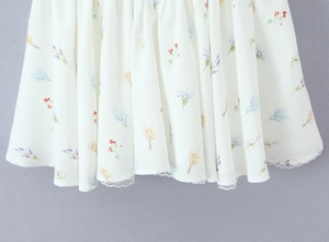 Dettaglio dell'orlo di un abito a fiori bianchi con pizzo delicato e motivi floreali colorati