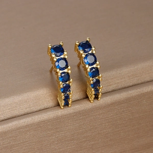 Close-up of gold C-shaped earrings set with round blue gemstones on brown fabric