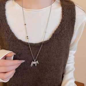 Détail d'un long collier argenté avec pendentif cheval et perles marron sur modèle