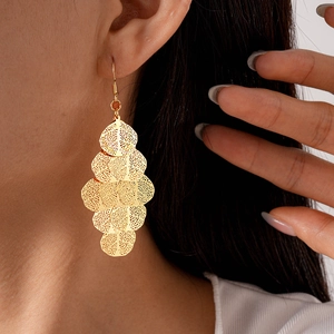 Close-up of golden geometric hollow tassel earrings worn by a model with a metallic finish