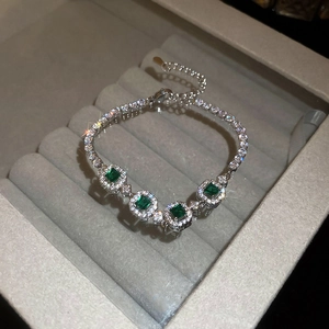 Macro detail of emerald-cut green stone bracelet with diamond halo on velvet base