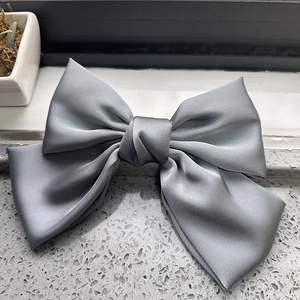Detail of grey satin silk bow hair clip showing smooth texture and layered design