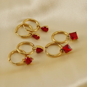Detail of three pairs of 18K gold earrings with red zircon in heart, square, and drop shapes