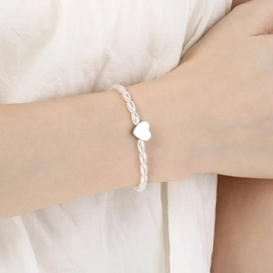 Detail of a pearl bracelet with heart charms on model against white pleated fabric