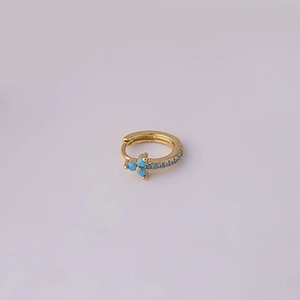 Close-up of golden hoop earring featuring a delicate blue beaded cross pendant detail