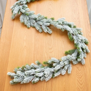 Lush snow-flocked green pine garland for Christmas decoration on a light wooden background