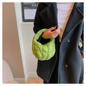 Detail of vibrant green quilted cloud bag worn over a black coat for street style look