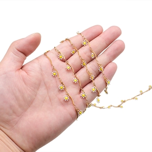 Detail of a wavy gold chain held in hand featuring white and yellow daisy charms