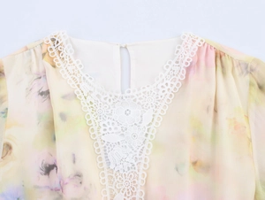 Dettaglio dello scollo in pizzo bianco su un abito in chiffon con stampe floreali