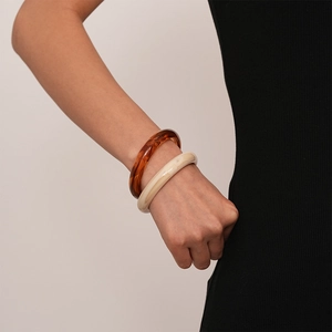 Close-up of amber brown and cream white wide resin bangles worn on the wrist