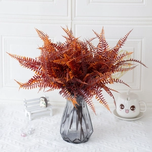 Artificial Persian fern in caramel orange color displayed in a gray geometric glass vase