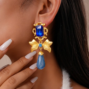 Close-up of vintage drop earring with blue stone, gold bow and marble drop on model
