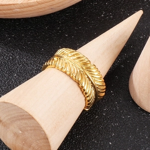 Detailed view of a golden leaf ring with feather texture on a wooden stand